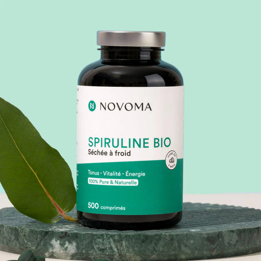 Pilulier de Spiruline Bio Novoma sur une pierre avec une feuille, fond vert