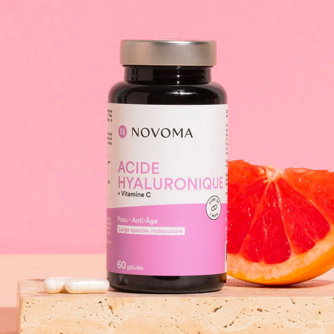 Pilulier d'Acide Hyaluronique Novoma avec un pamplemousse sur fond rose