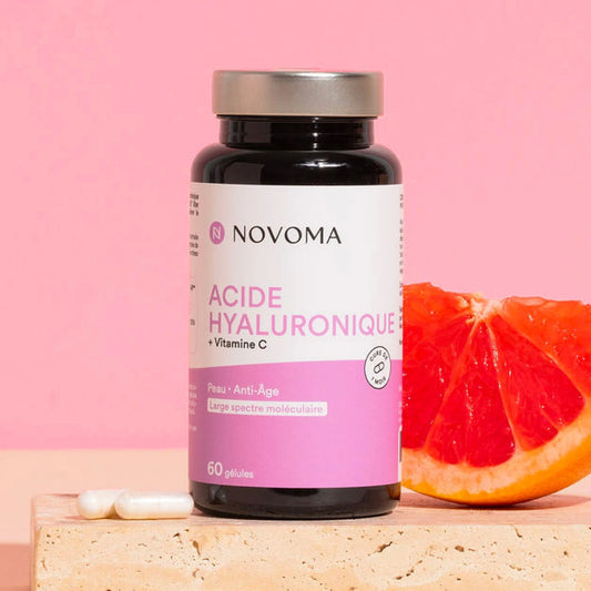 Pilulier d'Acide Hyaluronique Novoma avec un pamplemousse sur fond rose