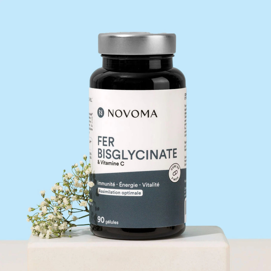 Pilulier de Fer Bisglycinate Novoma avec des fleurs blanches sur fond bleu