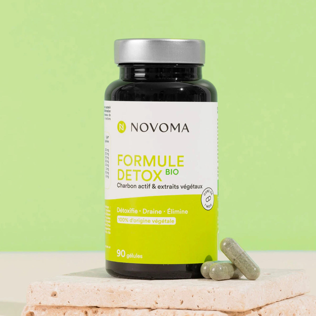 Pilulier de Formule Détox Bio Novoma sur une pierre, fond vert anis