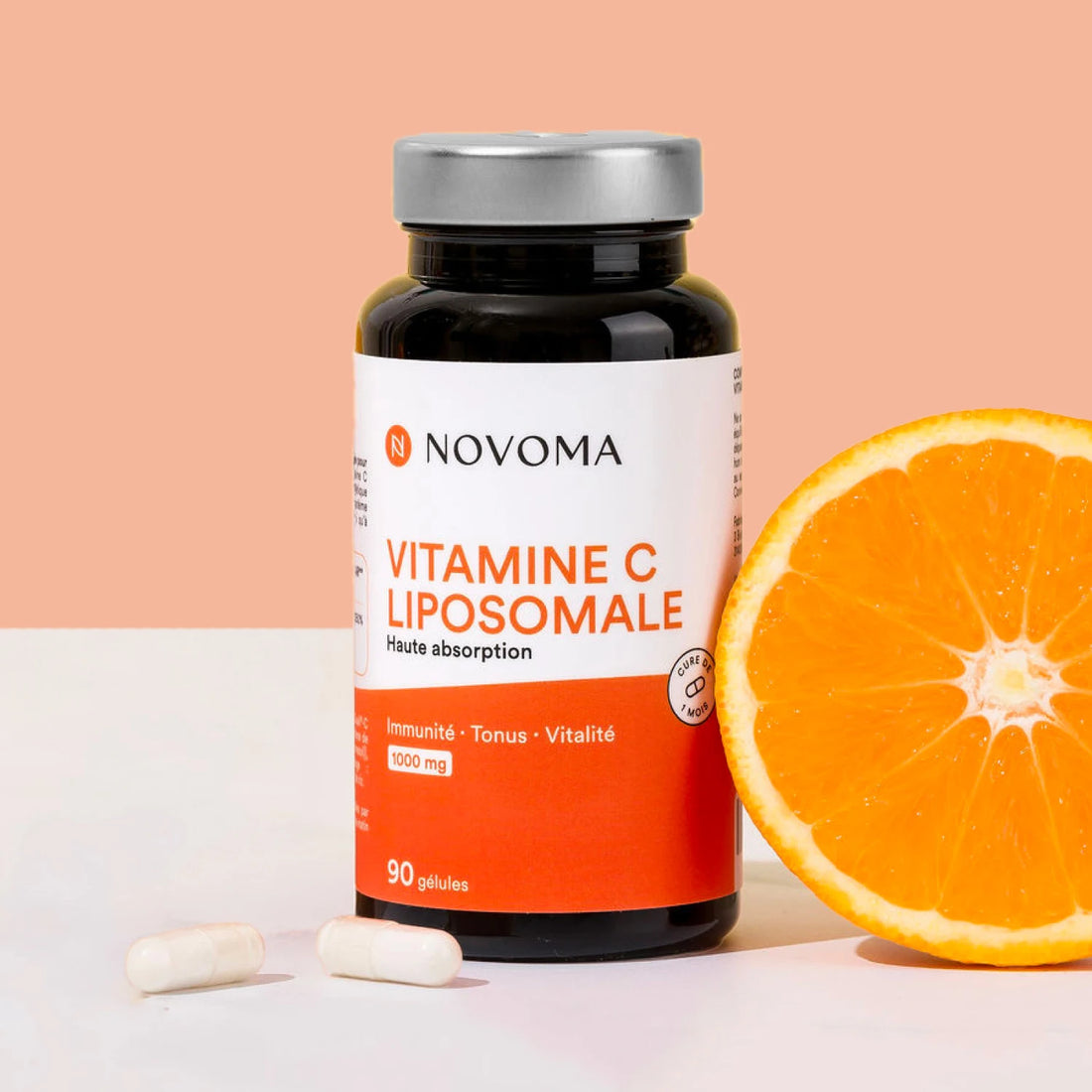 Pilulier de Vitamine C liposomale Novoma avec une demi-orange sur fond pêche