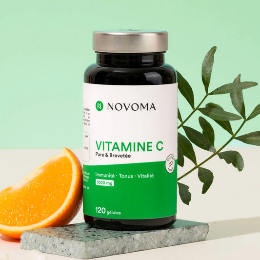 Pilulier de Vitamine C Novoma avec une orange et des feuilles sur fond vert