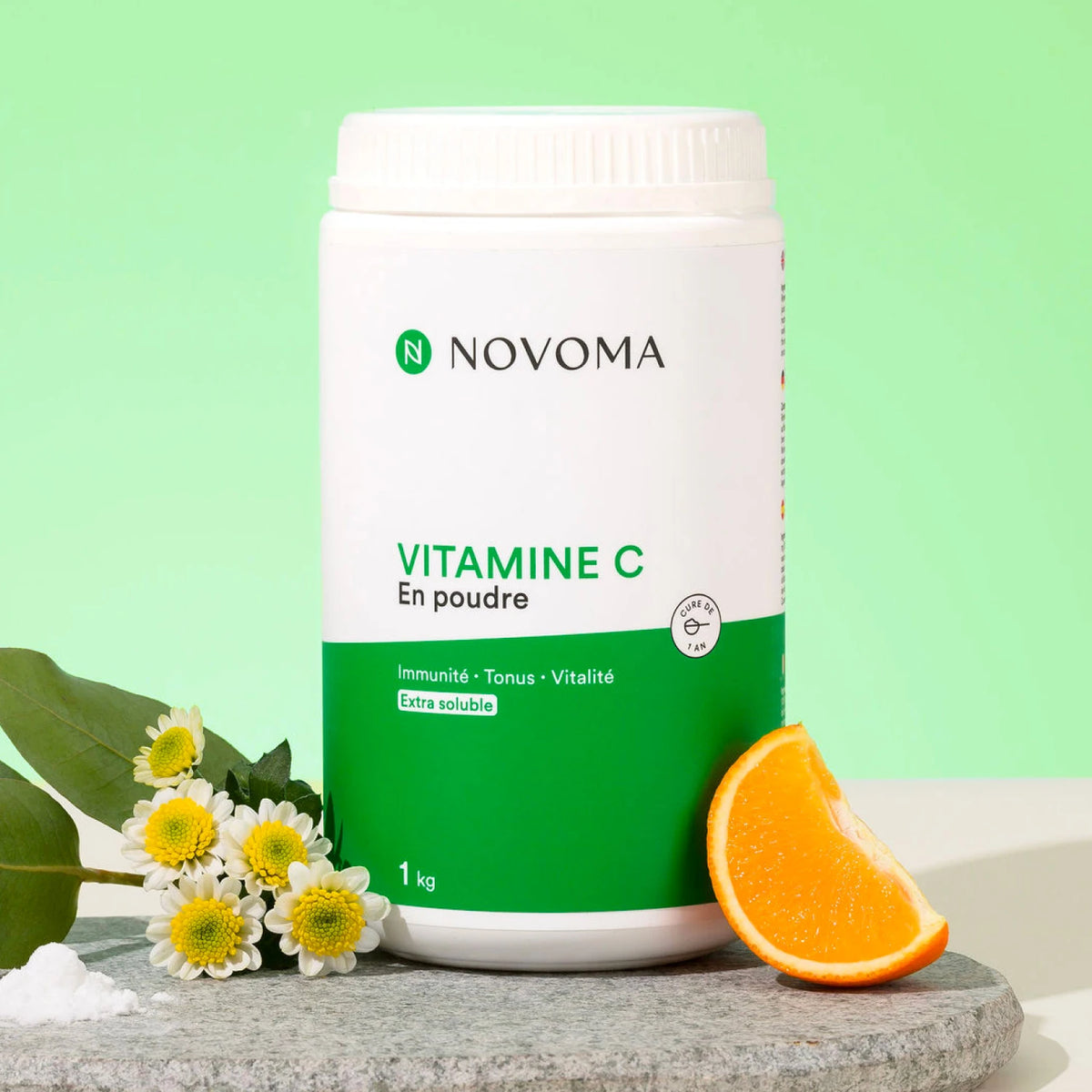 Pot de Vitamine C en Poudre Novoma avec une demi-orange et des fleurs sur fond vert
